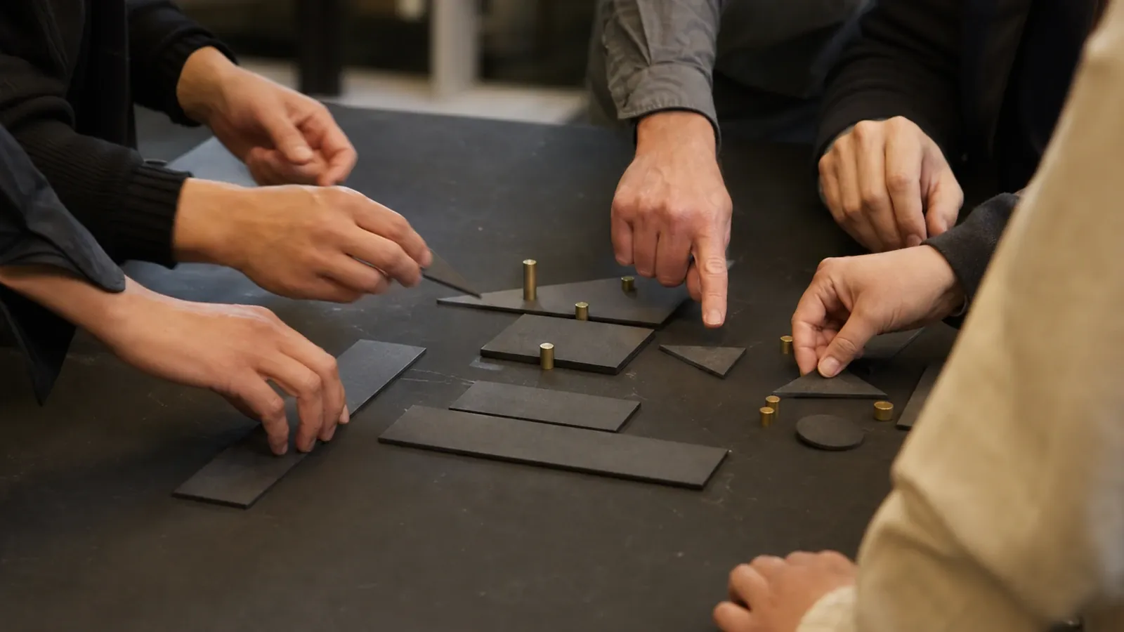 Several pairs of hands arranging dark and brass pieces across a worktable.